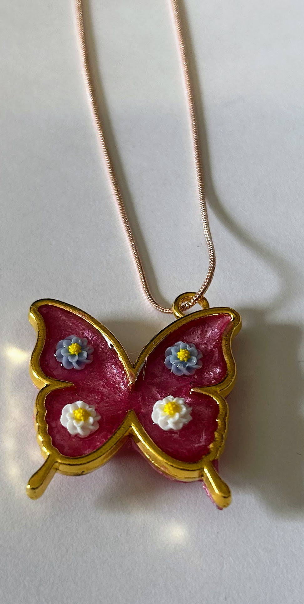 Necklace with pink butterfly gold tone frame with blue and white flowers on n 17" rose gold snake chain